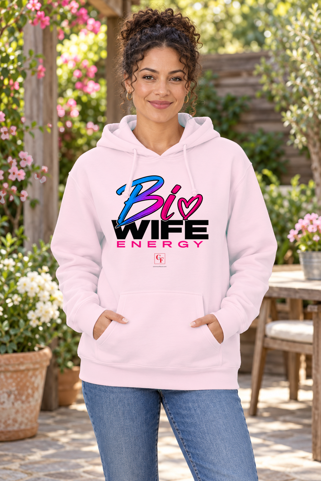 Woman wearing the Light Pink Bi Wife Energy hoodie in an outdoor lifestyle setting